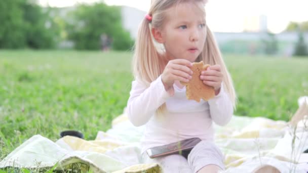 Une petite fille mange délicieusement du pain d'épice dans le parc au coucher du soleil