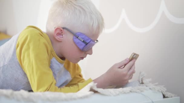 Ein Albino-Junge mit Brille liest zu Hause eine Nachricht auf seinem Handy — Stockvideo