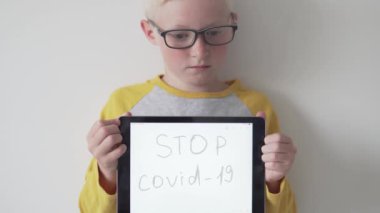 Gözlüklü üzgün çocuk elinde DUR Covid-19 yazıyor.