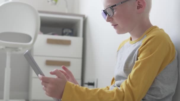 A boy with glasses with an occluder plays in a tablet at home — Stock Video