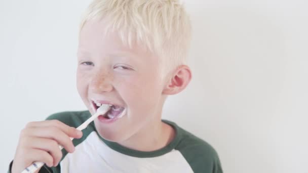 En tonårig pojke borstar tänderna med en tandkräm på vit bakgrund — Stockvideo