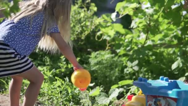 A little girl pours beds with vegetables water from childrens water — Stock Video