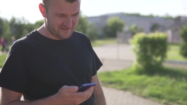 Мужчина использует мобильный телефон на улице во время прогулки в парке летом — стоковое видео