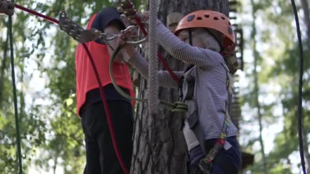A little girl in a helmet zips a carbine on the track in a rope park — Stock Video