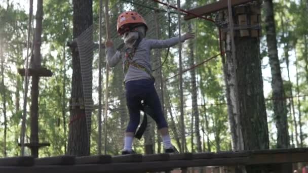 A little girl wearing a helmet on her head is being tested in a rope park on the street — Stock Video