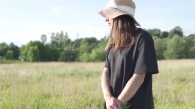 Bir buket kır çiçeğiyle şapkalı güzel bir kadın yazın tarlada yürüyor.