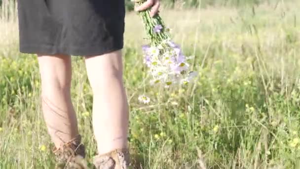 Eine Nahaufnahme von Frauenbeinen und einem Strauß Wildblumen während eines Spaziergangs auf dem Sommerfeld — Stockvideo