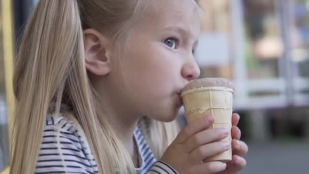 Een klein meisje eet 's avonds ijs op straat.. — Stockvideo