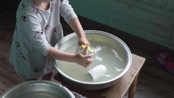 En liten flicka diskar i ett smutsigt bäcken i byn — Stockvideo