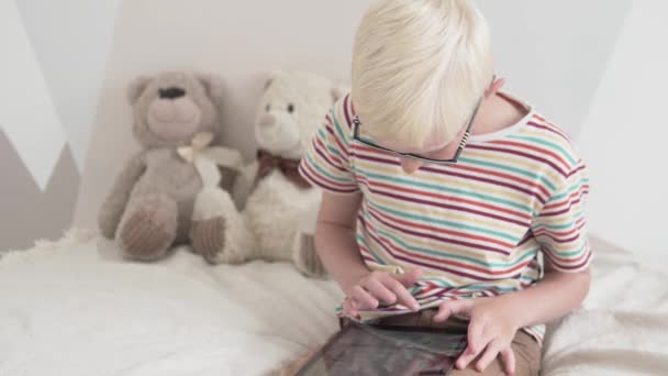 Hermoso chico rubio con gafas juega en la tableta en casa — Vídeos de Stock