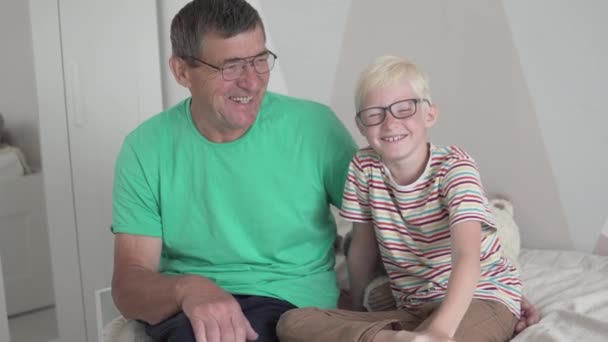 Een jongen met een bril praat thuis op de bank met zijn opa — Stockvideo