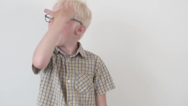 En rolig pojke med glasögon rynkar på håret på huvudet med handen. — Stockvideo