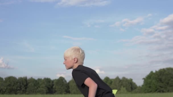 A handsome blonde boy launches a toy plane into the sky in the summer in a green field — Stock Video