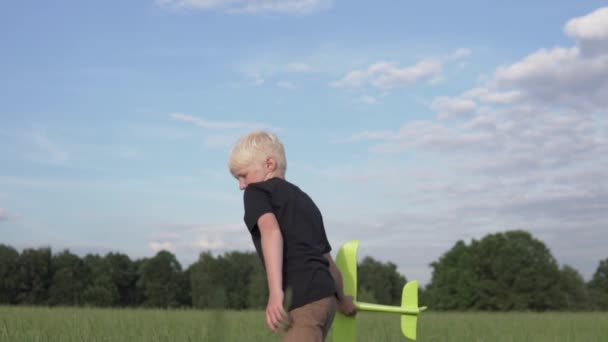 Um menino bonito lança um avião de brinquedo em um campo no verão — Vídeo de Stock