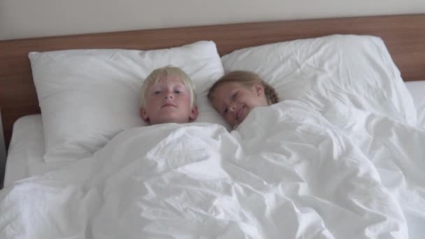 Gyerekek fiú és lány nevetnek az ágyban napközben aludni a szállodában — Stock videók