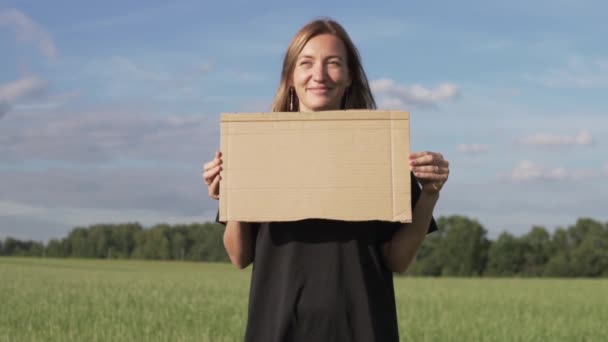 Красива жінка з картонним плакатом стоїть на полі влітку — стокове відео