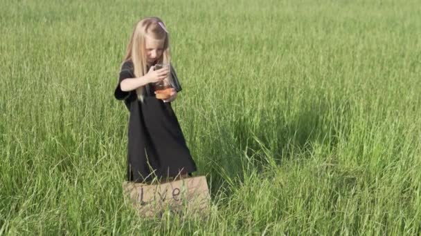 Una hermosa niña está en un campo con un póster y un reloj de arena — Vídeo de stock