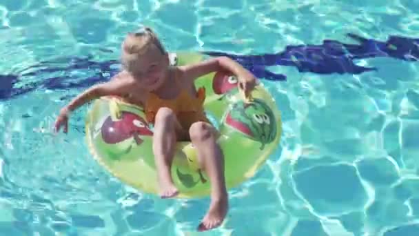 A beautiful little girl rides in an inflatable circle around the pool in the summer in the hotel — Stock Video