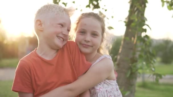 Close-up schattig blond jongen eerste kussen zijn vriendin in de wang bij zonsondergang — Stockvideo