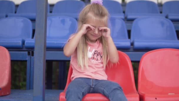 Mała dziewczynka płacze samotnie na trybunach stadionu sportowego — Wideo stockowe