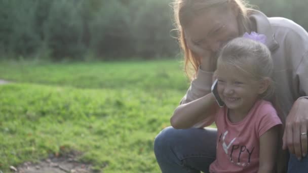 En liten flicka pratar i telefon medan hon går i skogen med sin mamma — Stockvideo