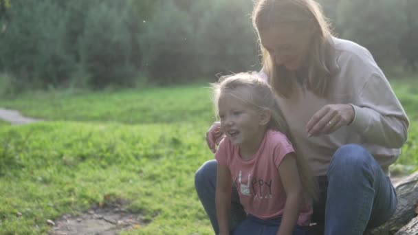 Mam en dochter zitten op een boomstam in het bos in de zomer bij zonsondergang. — Stockvideo