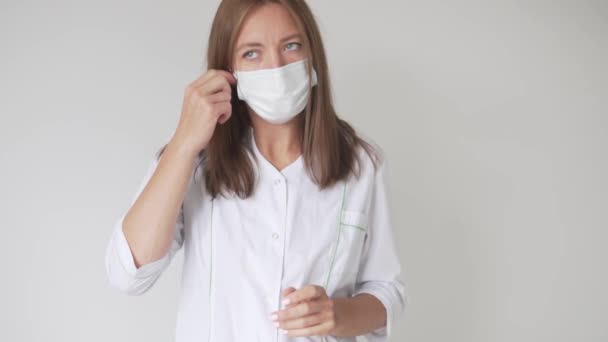 Piękna kobieta w medycznej sukni zdejmuje maskę medyczną z twarzy. — Wideo stockowe