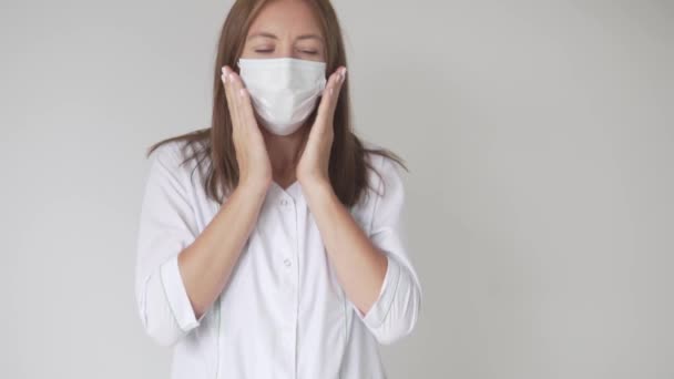 Una hermosa mujer con un vestido médico y una máscara en la cara tose — Vídeos de Stock