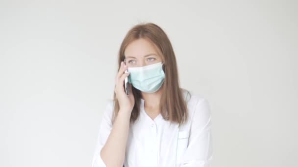 Een mooie vrouwelijke dokter met een medisch masker aan de telefoon. — Stockvideo