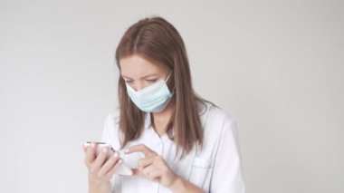 Yüzünde maske, elinde cep telefonu olan güzel bir kadın doktorun yakın çekimi.