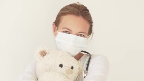 Nahaufnahme eines Kinderarztes in medizinischer Maske mit einem Teddybär in den Händen — Stockvideo