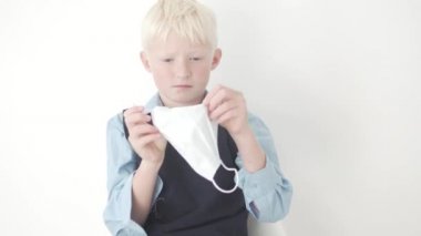Okul üniformalı güzel sarışın bir çocuk yüzüne tıbbi maske takıyor.