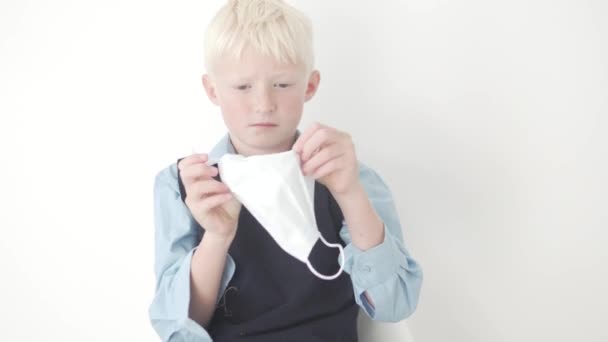 Krásný blonďatý chlapec ve školní uniformě klade lékařskou masku na jeho tvář — Stock video