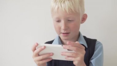 Sarışın çocuk oynamak için cep telefonu kullanıyor.