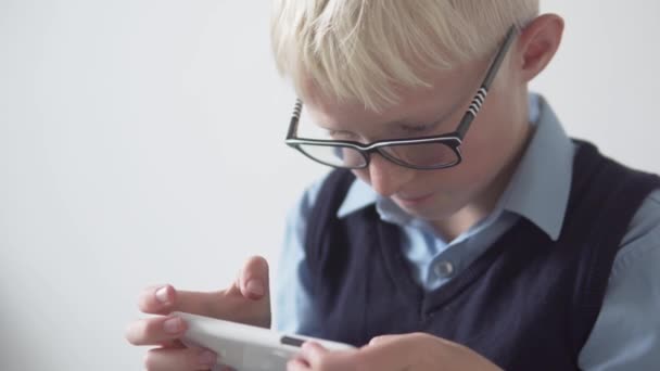 Un garçon avec des lunettes joue un jeu sur un téléphone portable à l'école à la récréation — Video