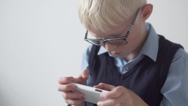 Un garçon blond avec des lunettes joue au jeu sur un téléphone portable. — Video