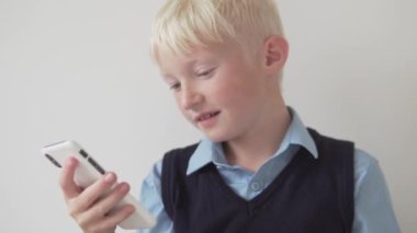 Sarışın bir çocuk teneffüste okulda cep telefonundan bir video izliyor.