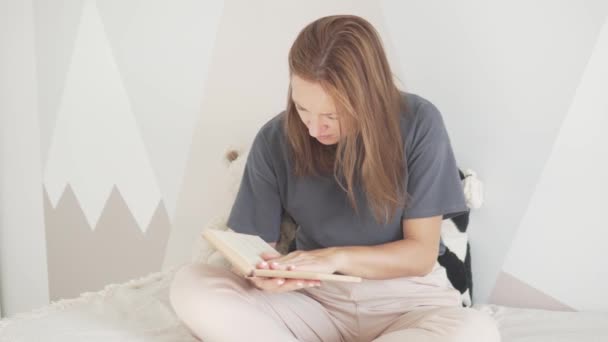 Egy gyönyörű nő könyvet olvas az ágyon. — Stock videók