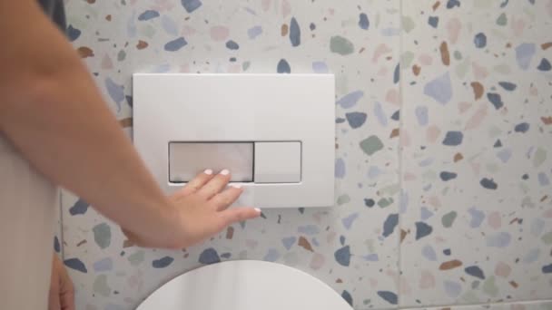 Een vrouw drukt op de witte spoelknop van het hangende toilet — Stockvideo