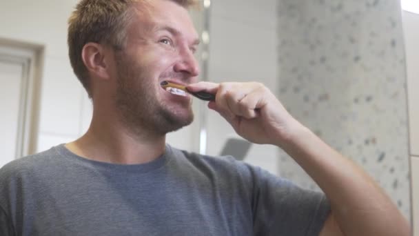 Hezký muž si ráno čistí zuby kartáčkem na zuby v koupelně.. — Stock video