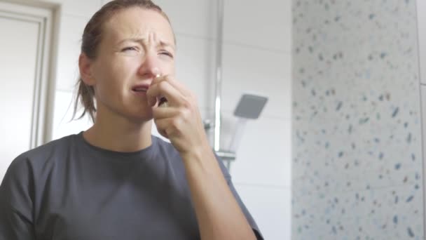 Una mujer lanza gotas en la nariz de la casa frente al espejo. — Vídeo de stock