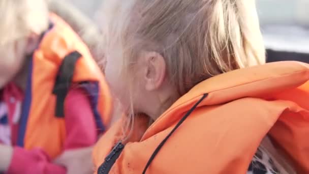 Uma menina feliz em um colete salva-vidas monta um barco a motor no rio — Vídeo de Stock