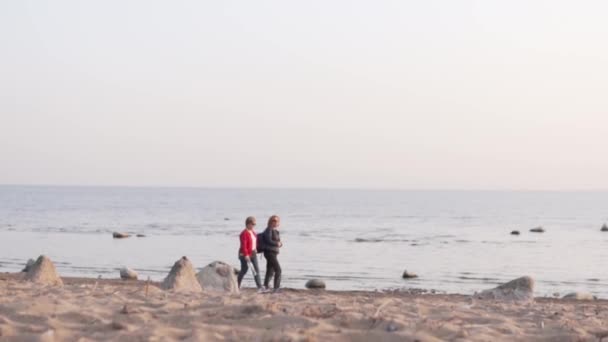 Two elderly female tourists walk along the sea in autumn — Stock Video