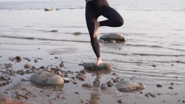 Жінка стоїть в позі дерева на камені біля моря — стокове відео