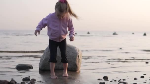 Bambina gioca nella sabbia sulla spiaggia in riva al mare in autunno — Video Stock