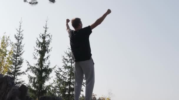 Mannen är jublande och sträcker upp händerna i en bergsvandring efter uppstigningen — Stockvideo
