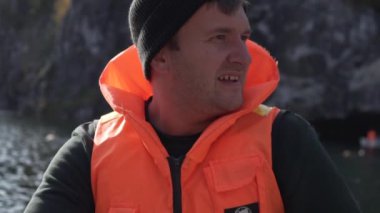 Can yeleği giymiş bir adamın yakın çekimi göldeki bir teknede yüzüyor.