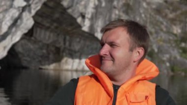 Can yeleği giymiş mutlu bir adam bir dağ gölünde bir teknede yüzer.