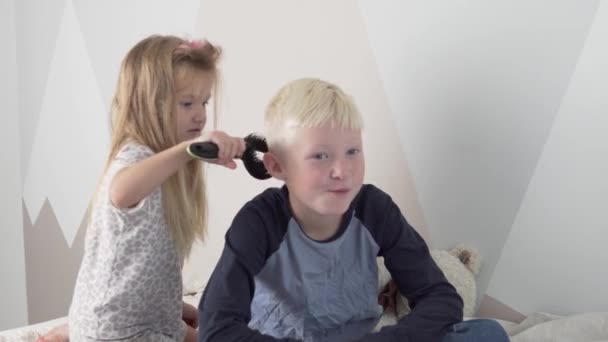 有趣的小妹妹把金黄色的头发梳理到她哥哥的头上 — 图库视频影像