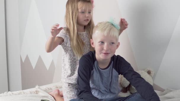 Het meisje vlecht haar haar en steekt haar oudere broers haar — Stockvideo